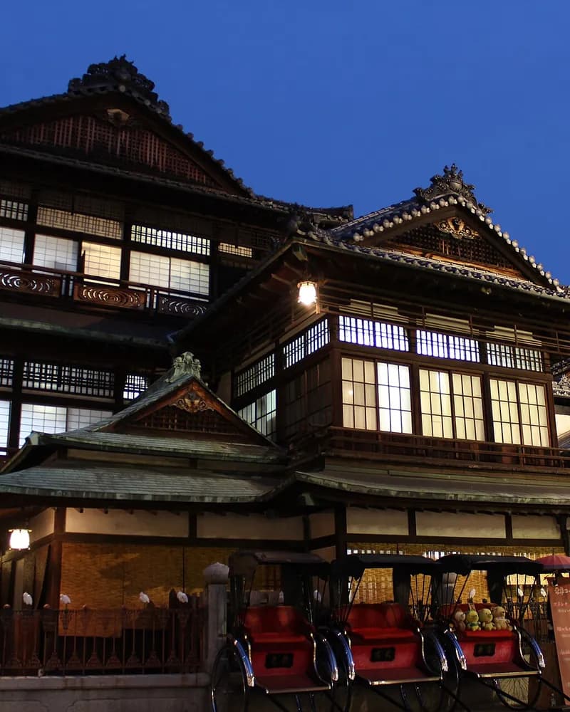 The three-storey wooden Dogo Onsen Honkan bathhouse lit at dusk