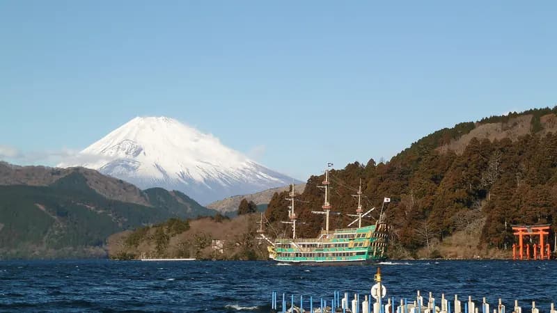 Mount Fuji above Lake Ashi in Hakone, with a sightseeing cruise ship and the red torii of Hakone Shrine on the shore