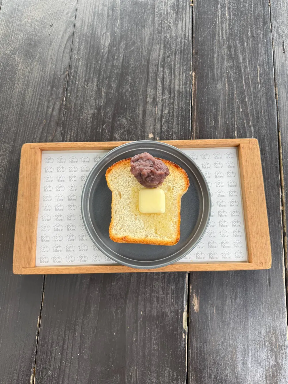A slice of toast with butter and sweet red bean paste on a wooden tray at Café La Ruche